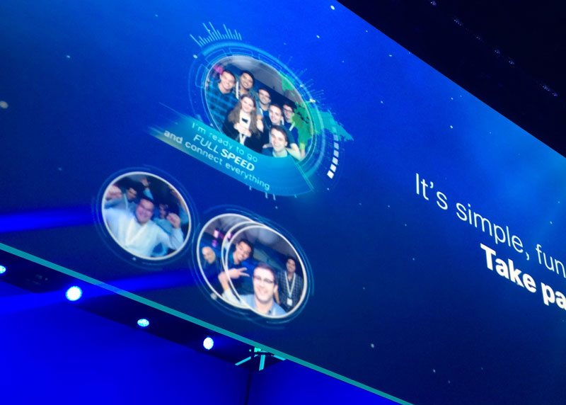 Big screen above the show floor displaying attendee photos and their Full Speed commitments