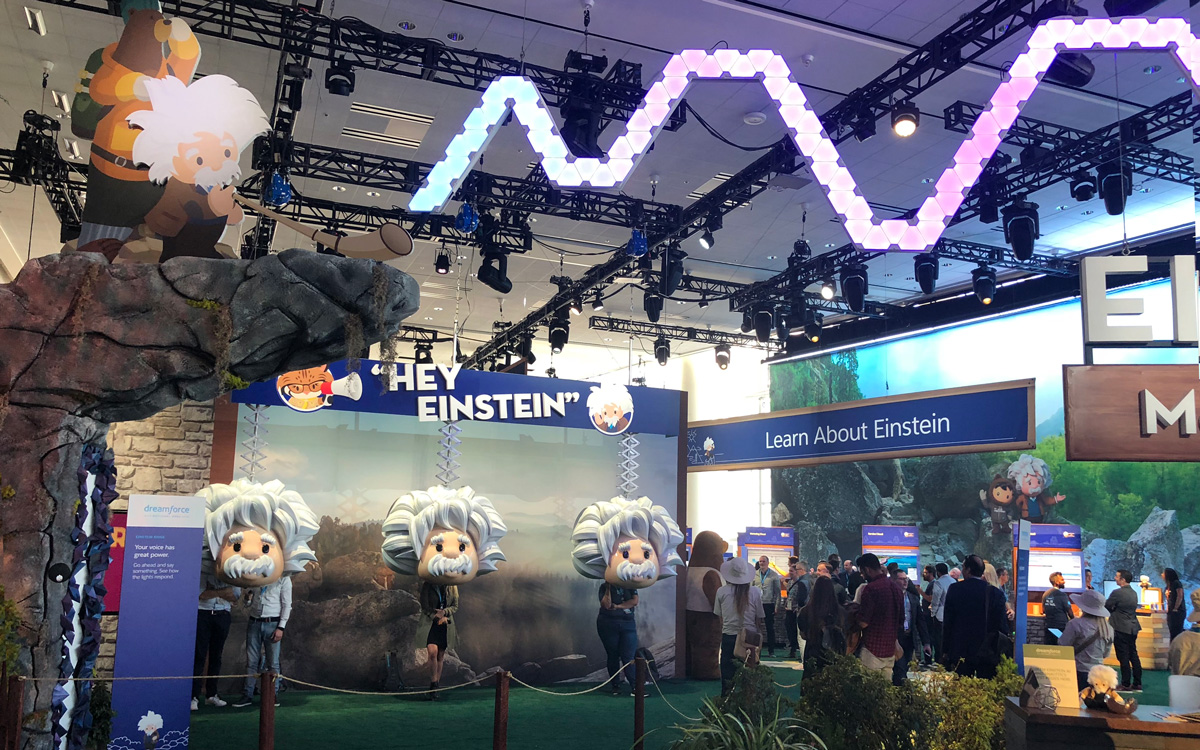 Wide view of the Hey Einstein booth with signage and lighting rig on the Dreamforce show floor